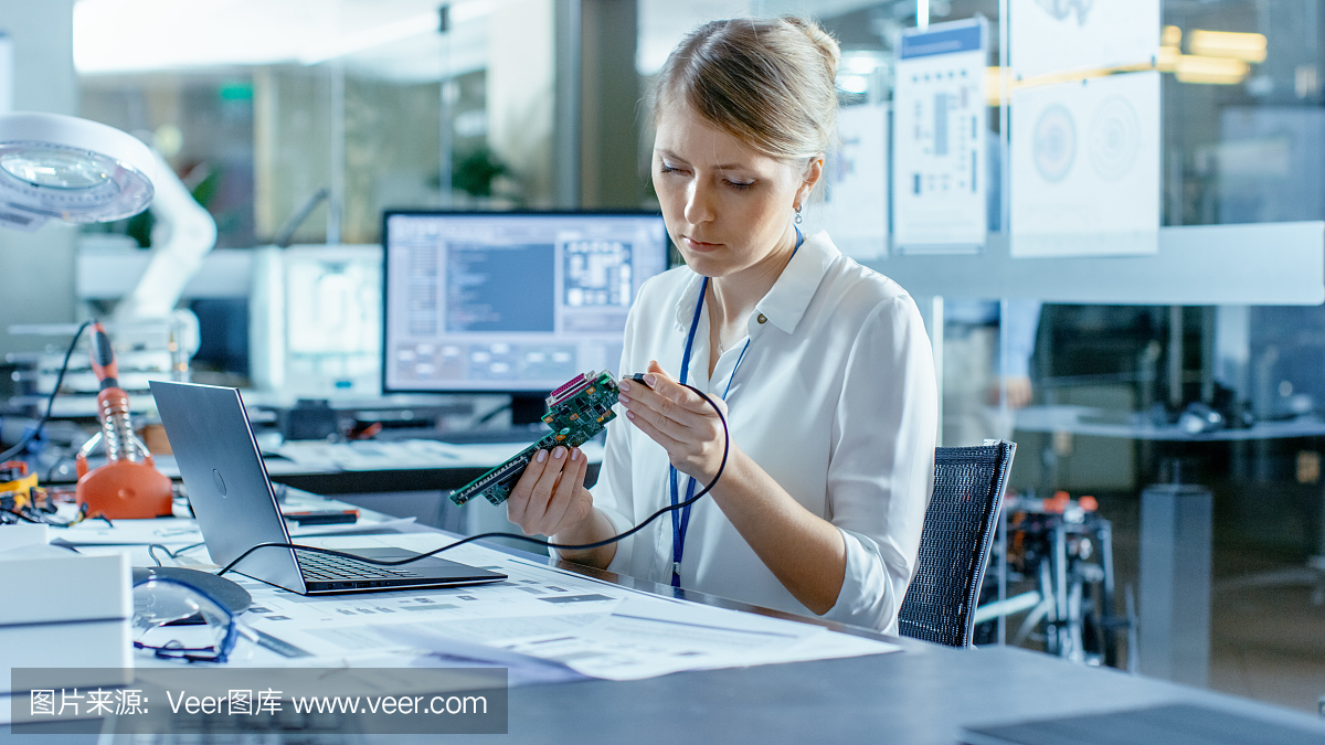 女计算机科学家将电路板连接到她的笔记本电脑并开始编程。她在先进技术实验室工作。